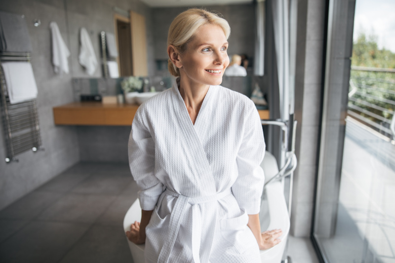Elderly woman smiling in luxury walk-in shower suite in Chichester, showcasing safe and accessible design.